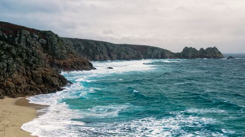 Free A stunning view of a rocky coastline with crashing turquoise waves under an overcast sky. Stock Photo