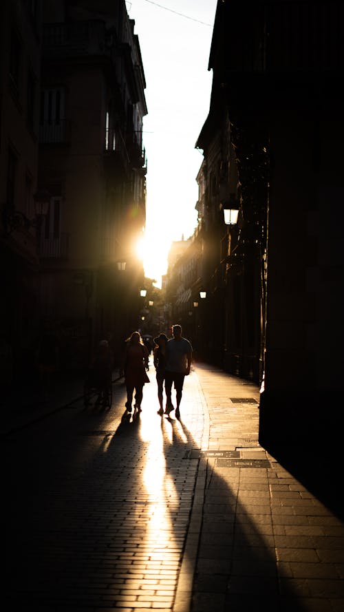 Silhouettes of People Walking between Buildings in City at Sunset