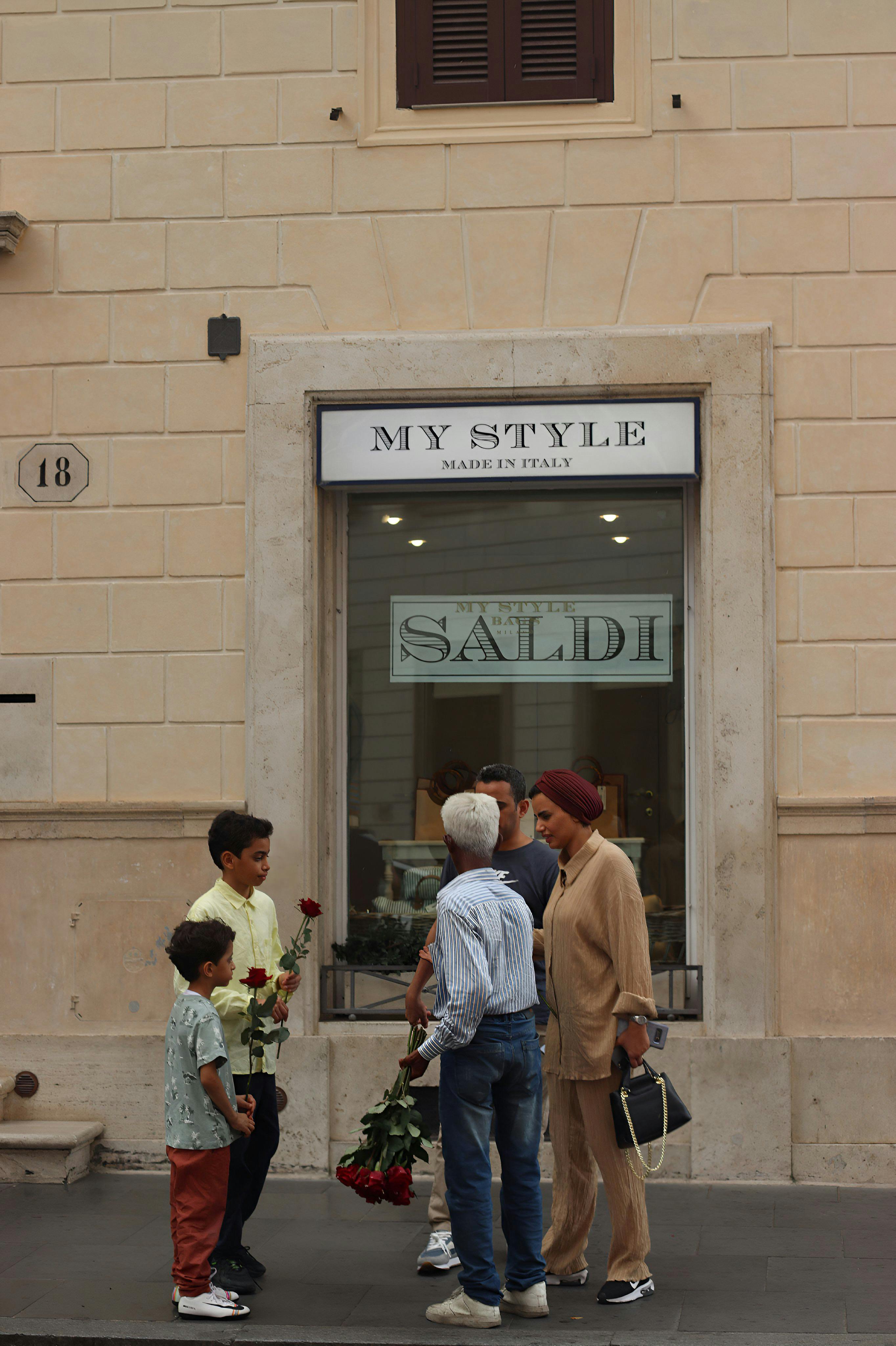 A family gathers with flowers in front of a boutique in Rome, Italy, capturing urban charm and culture.