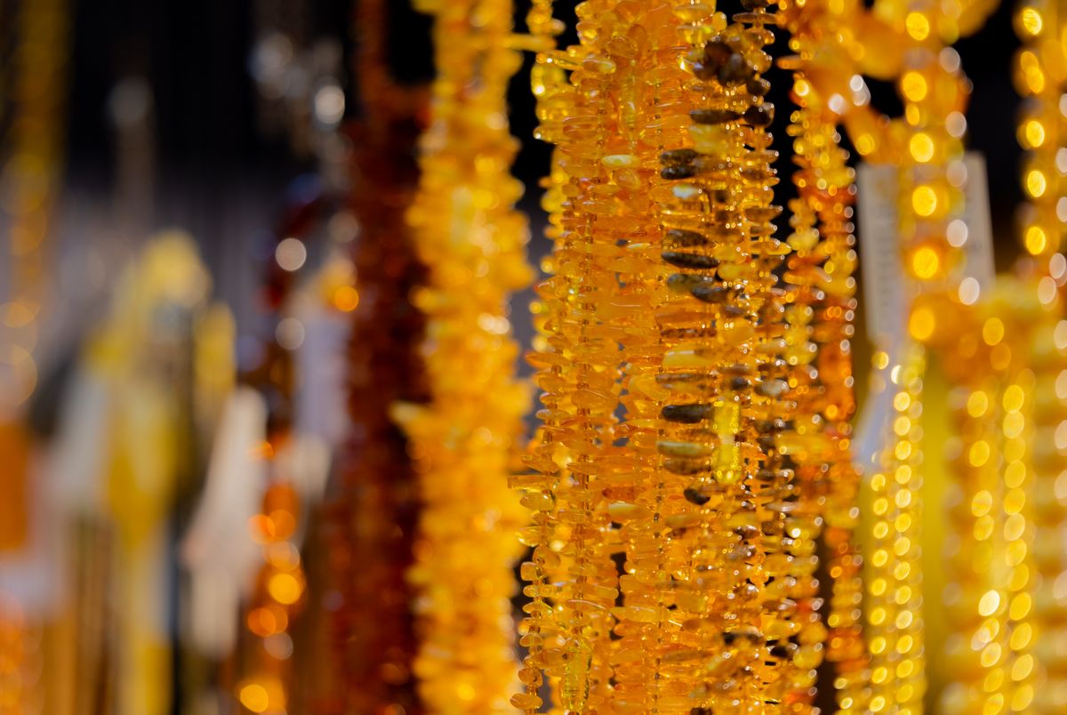 Rows of golden-orange amber necklace strands hanging on display at a Mariacka Street market stall, warm light catching the beads.