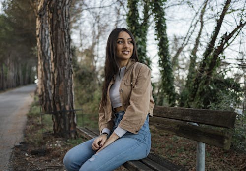 Smiling Brunette Woman in Jacket Sitting on Bench in Park