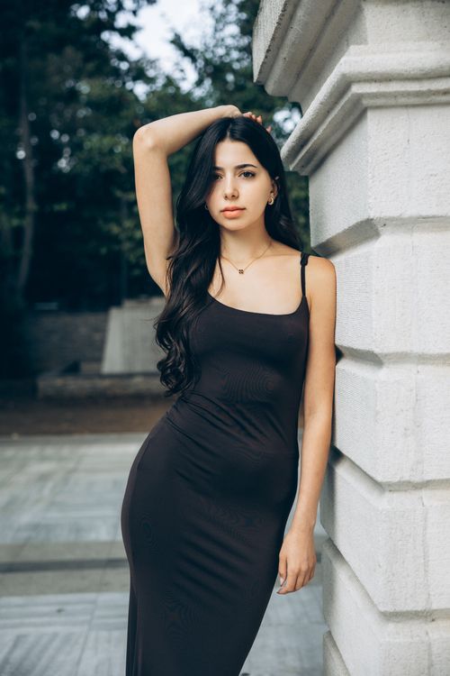 Free Elegant woman in a black dress posing against a stone pillar outdoors in Türkiye. Stock Photo
