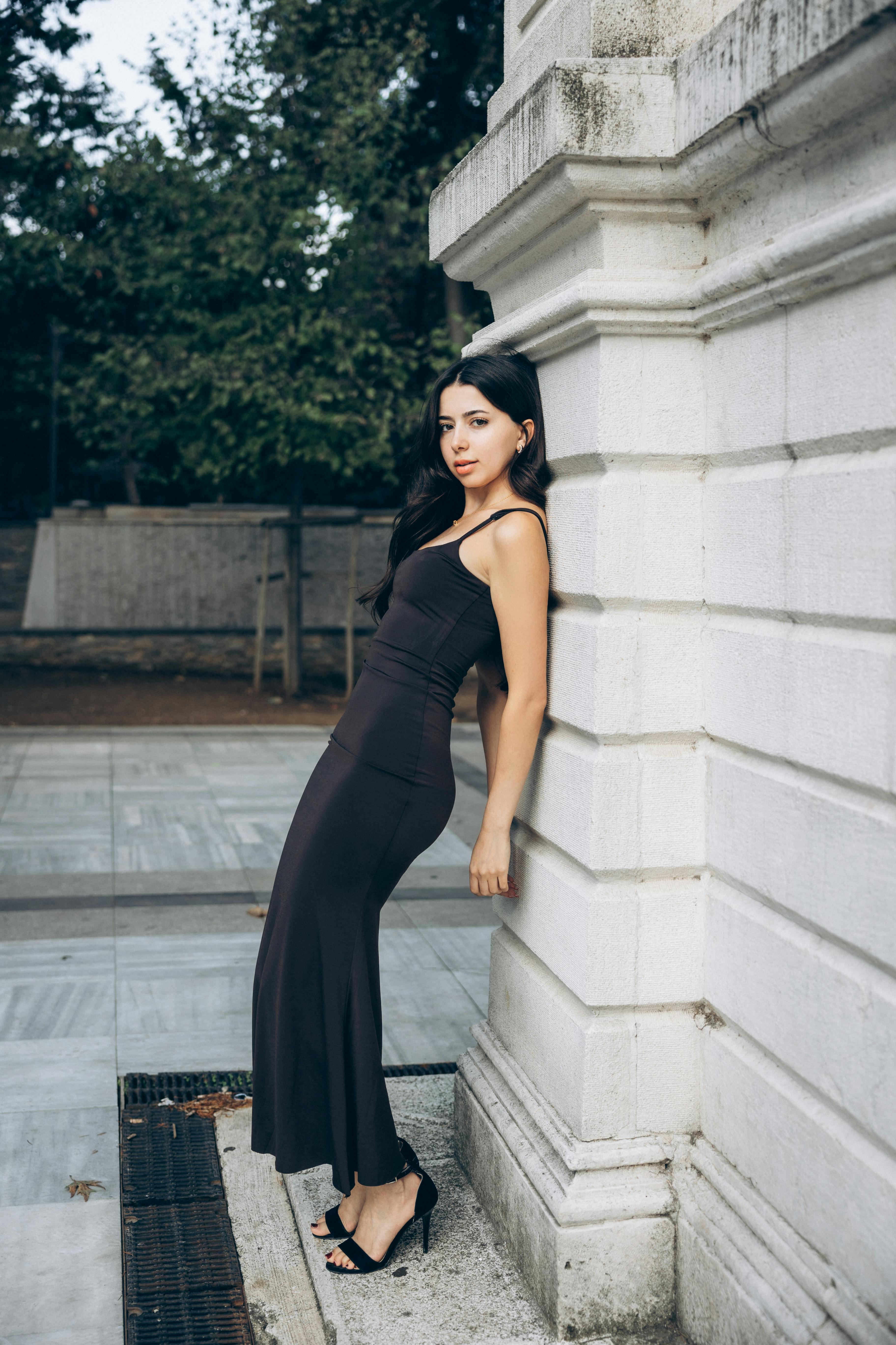 a woman in a black dress leaning against a wall