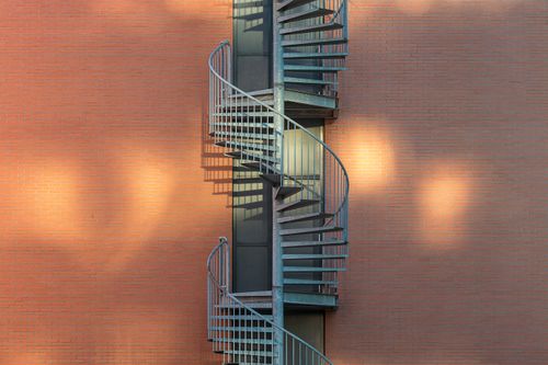 Free Elegant spiral metal staircase on a brick building facade illuminated by warm sunrise light. Stock Photo