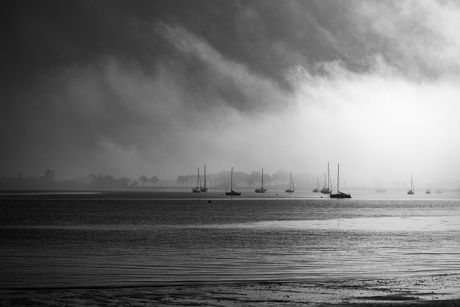 Black and white photo of sailboats in a misty seascape creating a serene atmosphere.