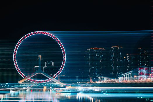 A ferris wheel beautifully illuminated in a bustling city skyline, showcasing vibrant night-time motion and lights.