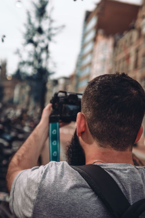 Free A man takes a photo in a bustling urban street with buildings in the background. Stock Photo