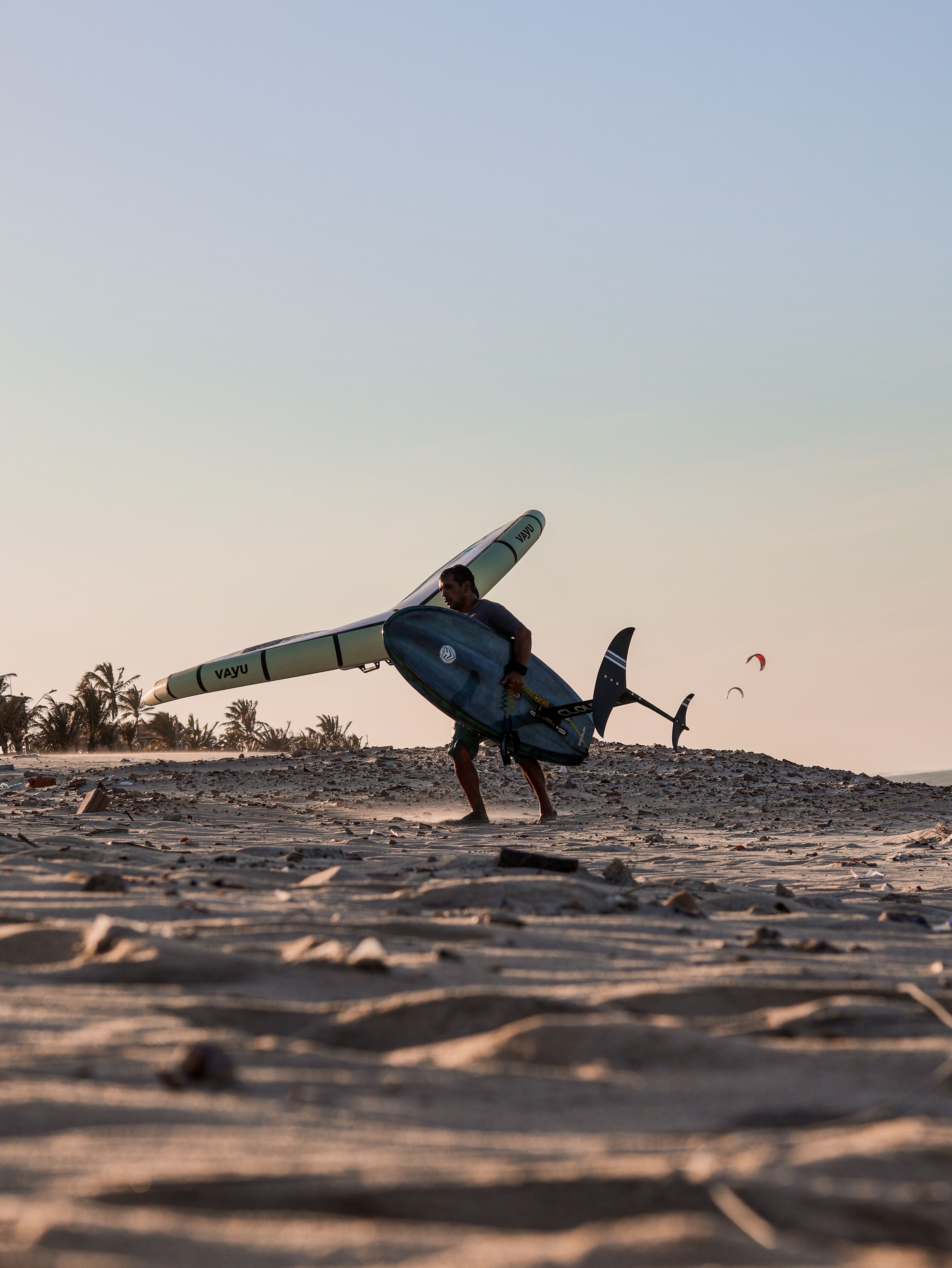 A man walks on a sandy beach carrying a surfboard during a beautiful sunset.