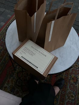 Brown paper bags and a delivery box on a round table with a rug.