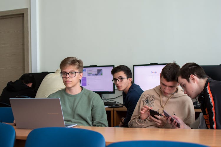 Teenagers Sitting With Smartphones And Computers In Classroom