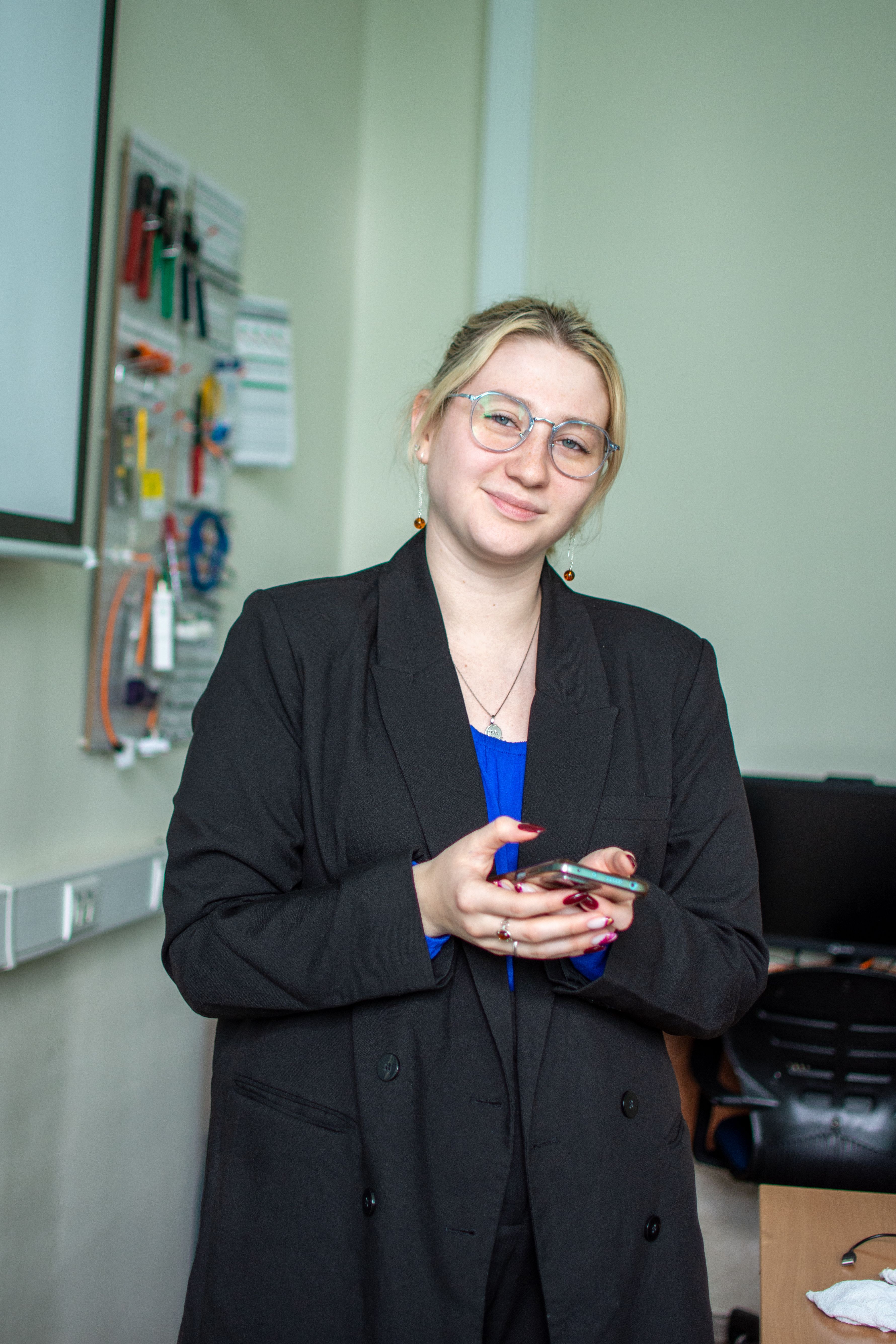 Confident businesswoman in a black suit holding a smartphone indoors, showcasing elegance and professionalism.