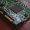 A macro close-up of a prominent black microchip mounted on a green computer circuit board.