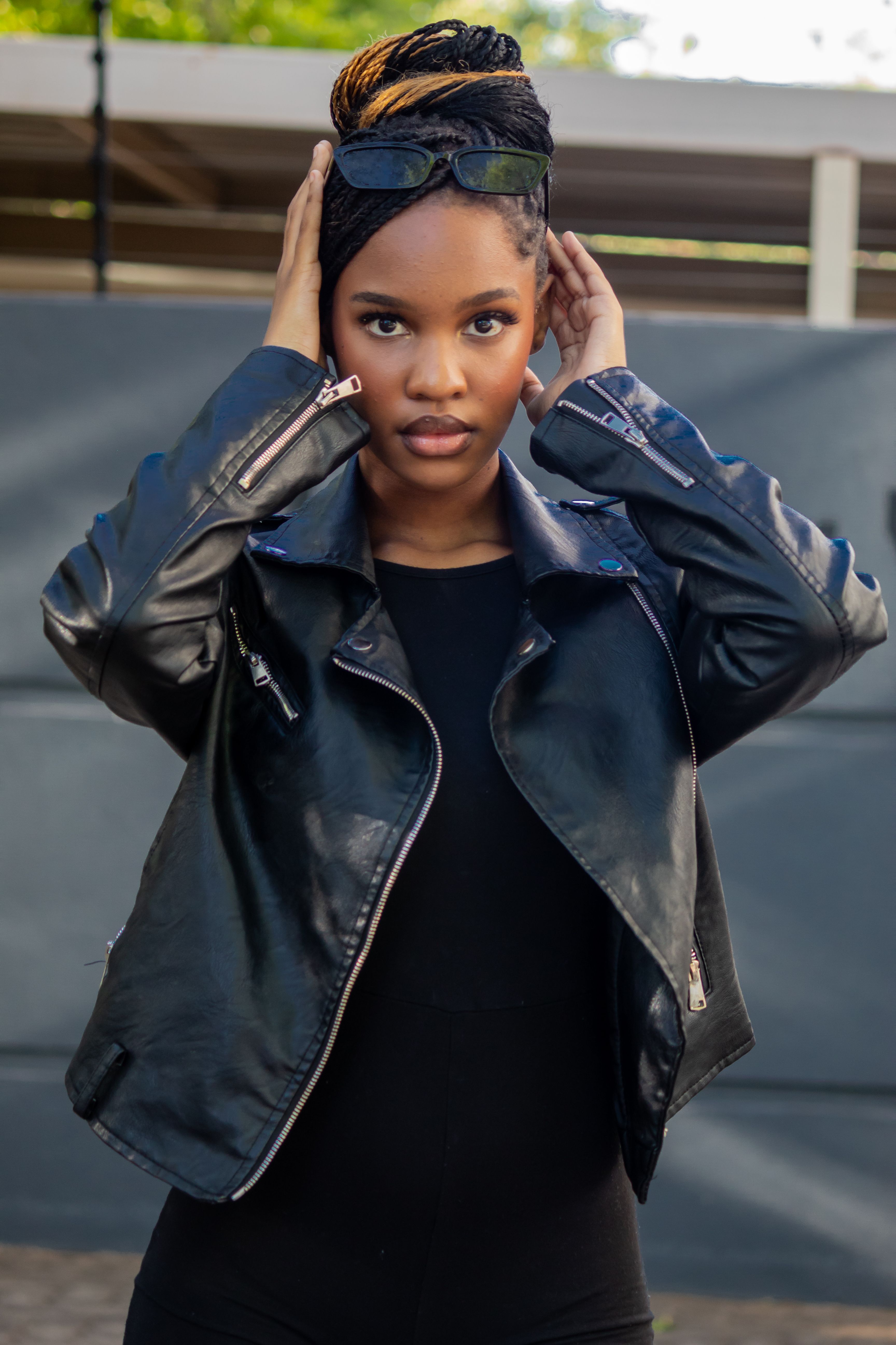 Fashionable portrait of a woman in a black leather jacket with sunglasses, outdoors.
