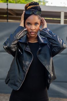 Fashionable portrait of a woman in a black leather jacket with sunglasses, outdoors.