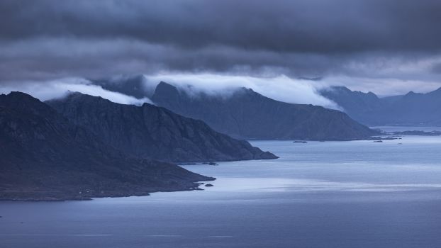 Mysterious moody blue landscape of fjords and mountains in the Nordic region under heavy clouds.