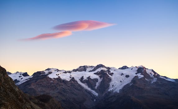 Stunning mountain peak at sunrise with pink clouds and snow-capped peaks, perfect for nature and travel inspiration.