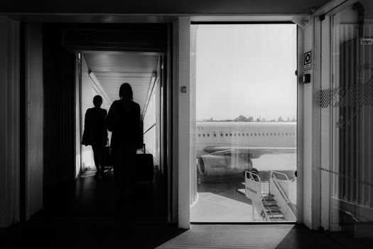 Black and white image of travelers boarding an airplane through the terminal.