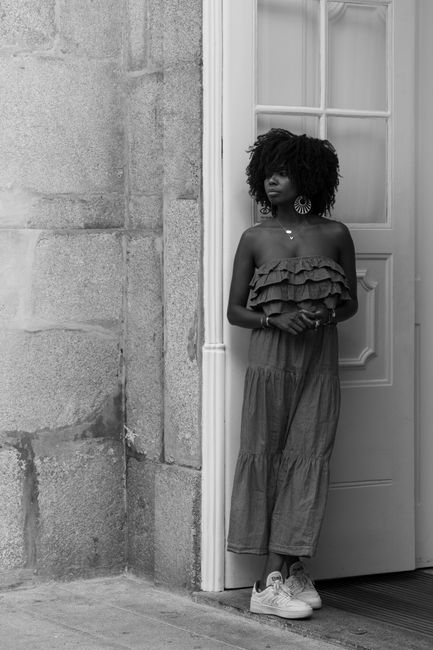 Stylish woman in ruffled dress leans against a white door in a black and white photo.