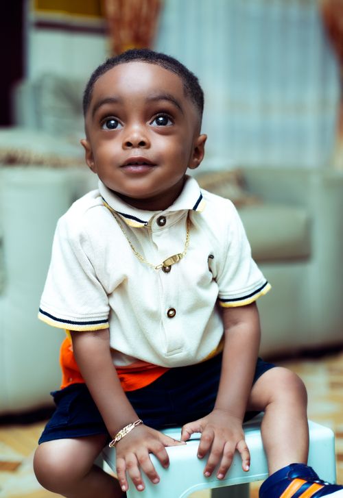 Free Adorable toddler wearing jewelry sits indoors in Kumasi, Ghana, capturing a joyful and stylish moment. Stock Photo