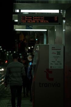 A man walking at a tram stop in Cuenca, Ecuador at night with city lights and digital signage.