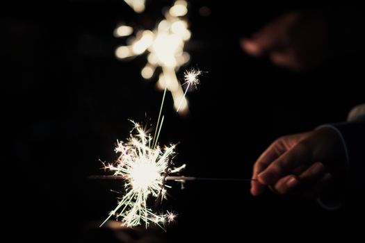 Close-up of hands holding sparklers, illuminating a night-time celebration.