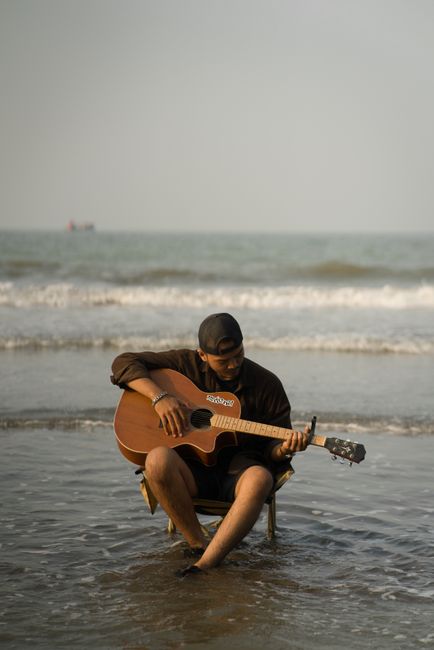 A man sits playing an acoustic guitar at the seaside in Jawa Tengah, Indonesia, creating a serene musical moment.