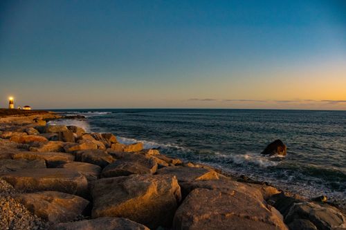 Free Serene sunset view over rocky coastline and lighthouse in Narragansett, RI. Stock Photo