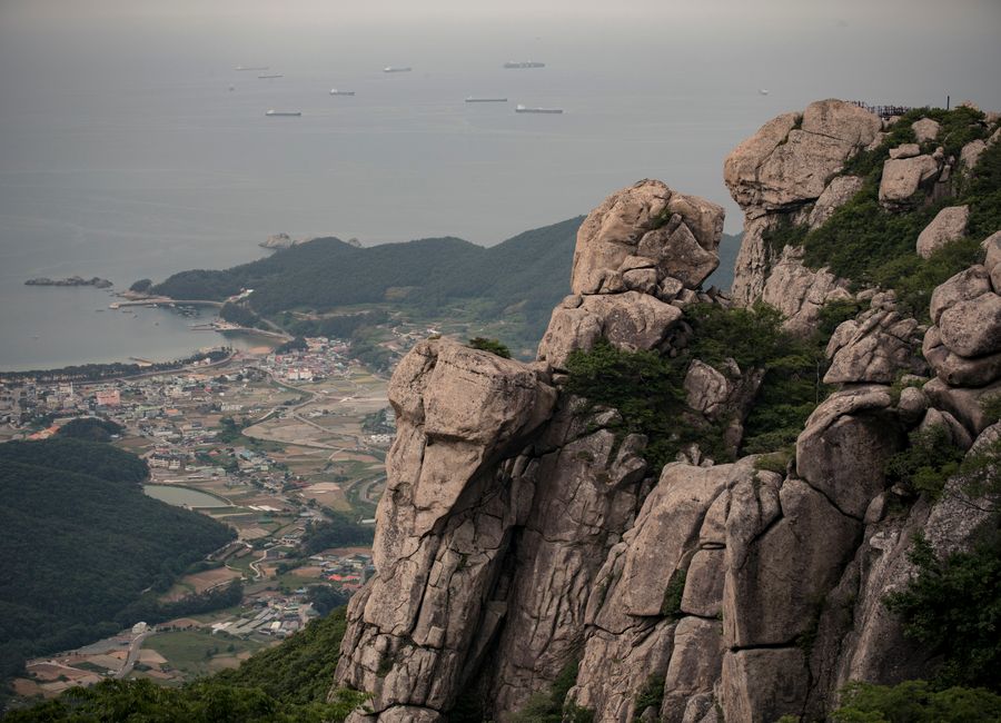 Breathtaking aerial view of rugged coastal mountains overlooking a quaint seaside town and expansive sea.