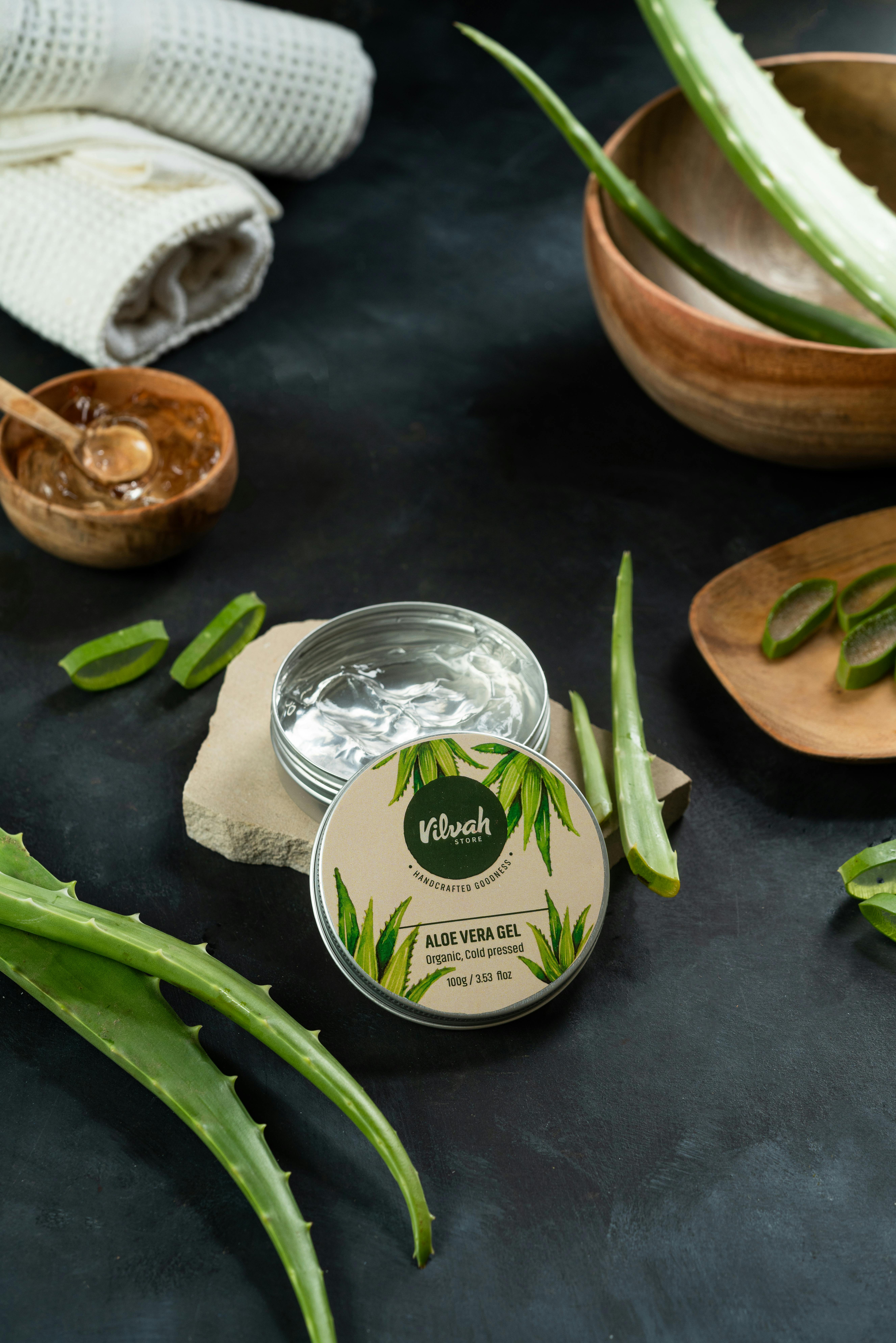 Aloe vera gel jar surrounded by fresh aloe leaves and spa items on a dark surface.