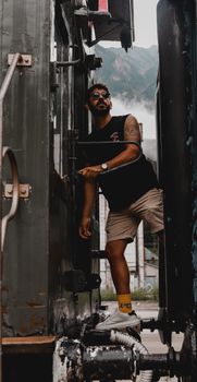 A man in casual summer attire poses confidently on a train, exuding a rugged, adventurous vibe.