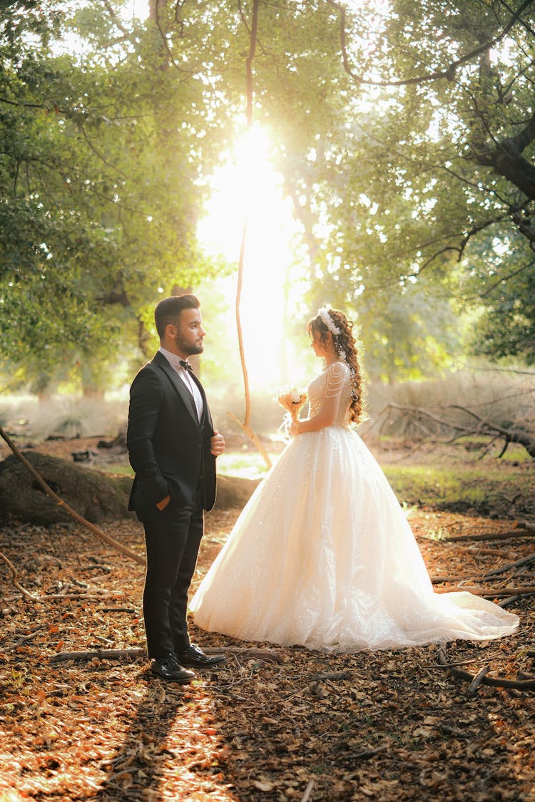 Groom And Bride Standing Apart In The Forest In The Sunlight