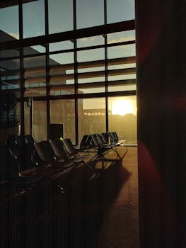 Empty airport lounge chairs by large windows during sunrise creating a peaceful ambiance.
