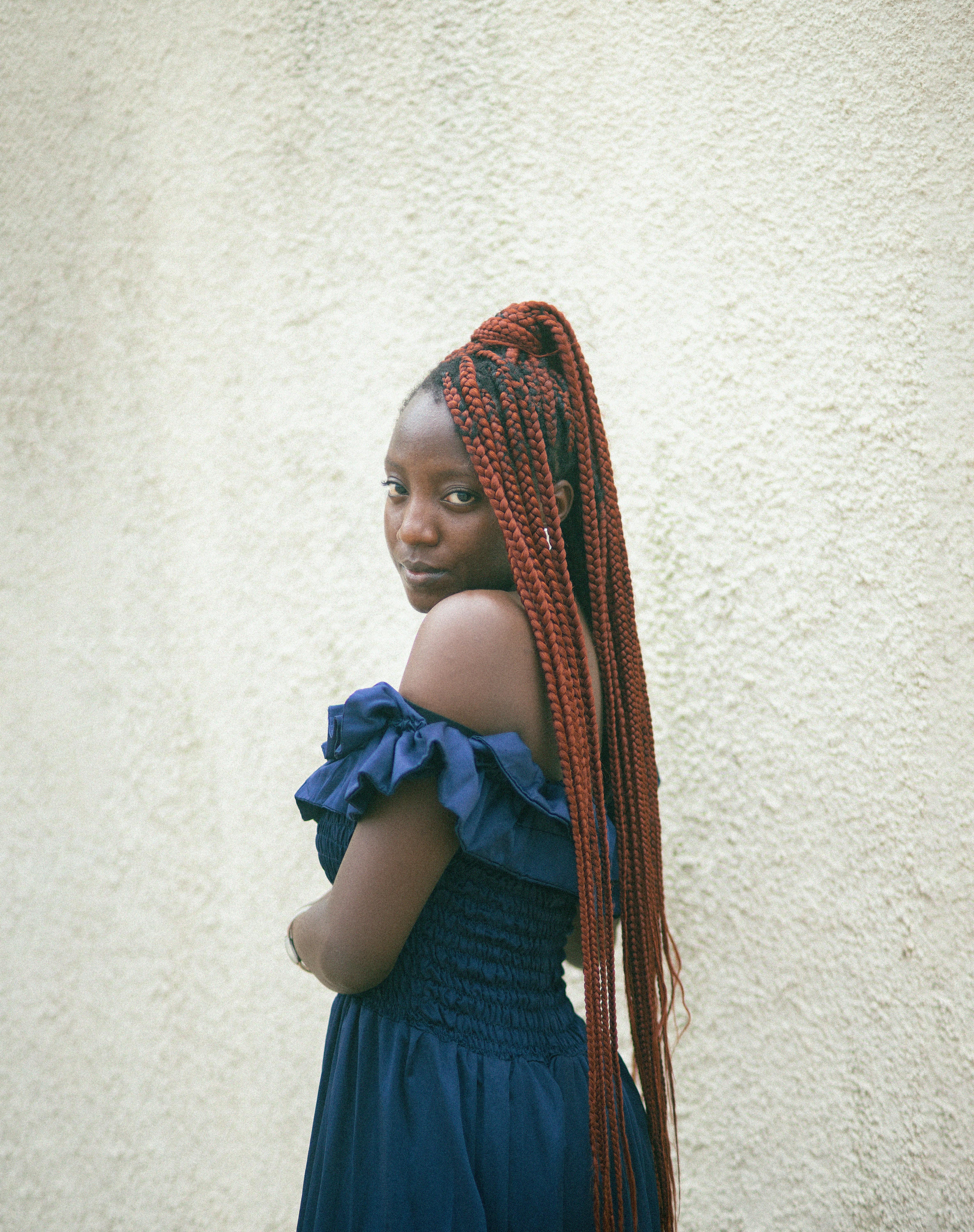 Fashion model in Abuja wearing a blue dress, showcasing long braided hair against a textured wall.