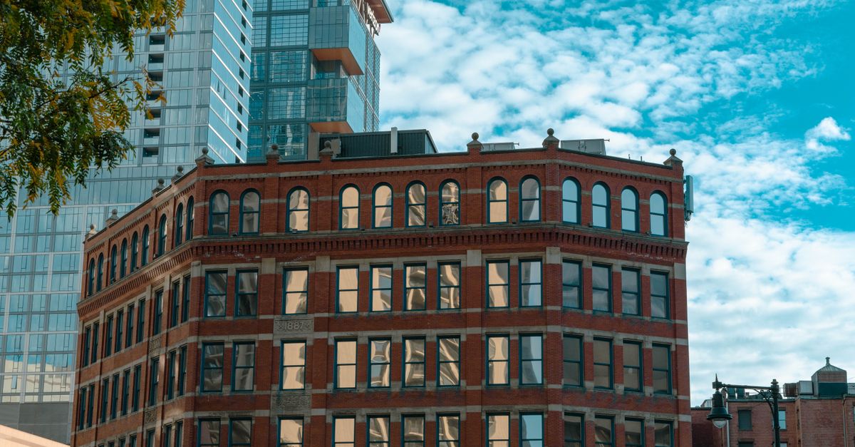 A historic brick building juxtaposed with modern glass skyscrapers in a vibrant cityscape.