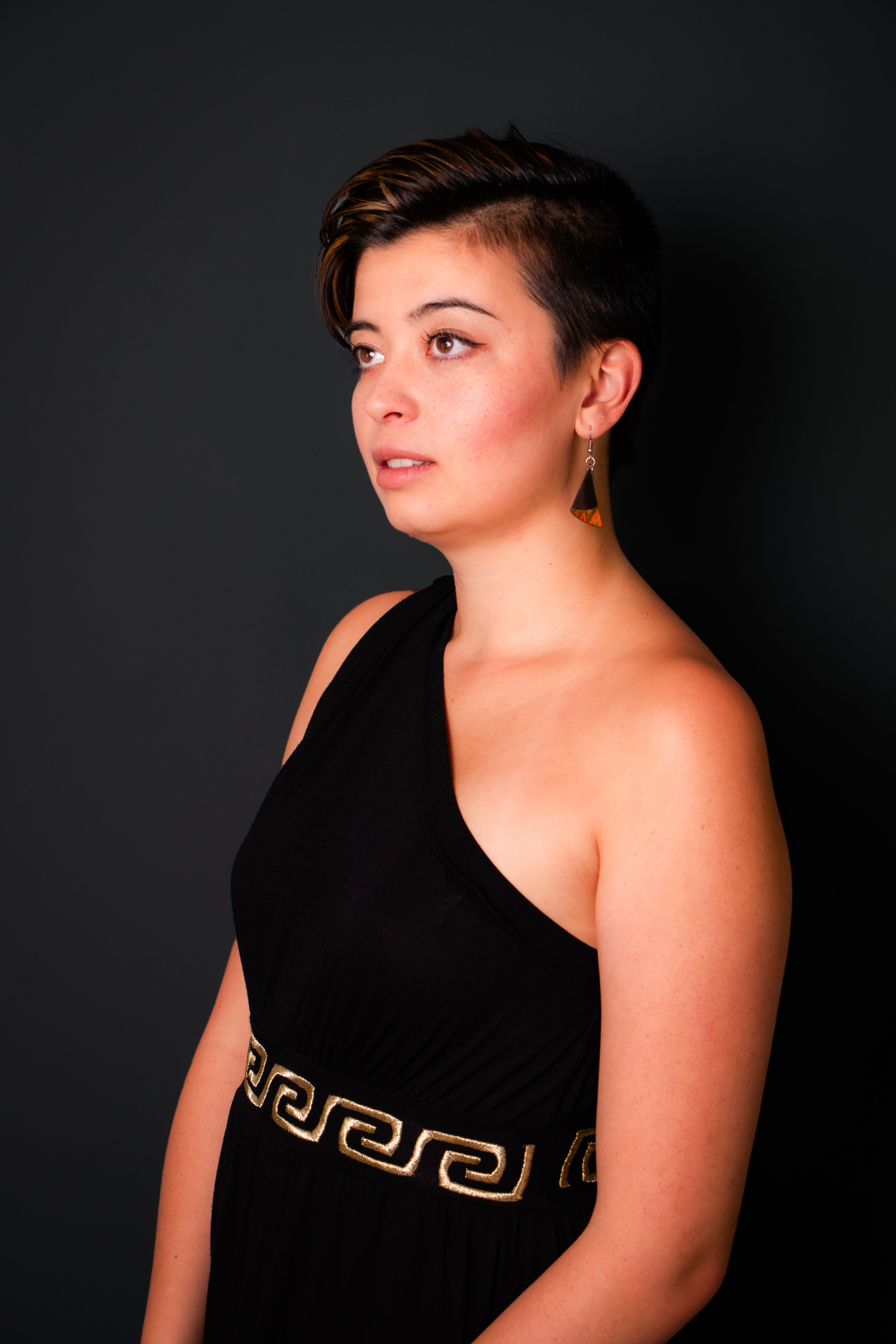 Portrait of a stylish woman in a black dress with geometric earrings, against a dark background.