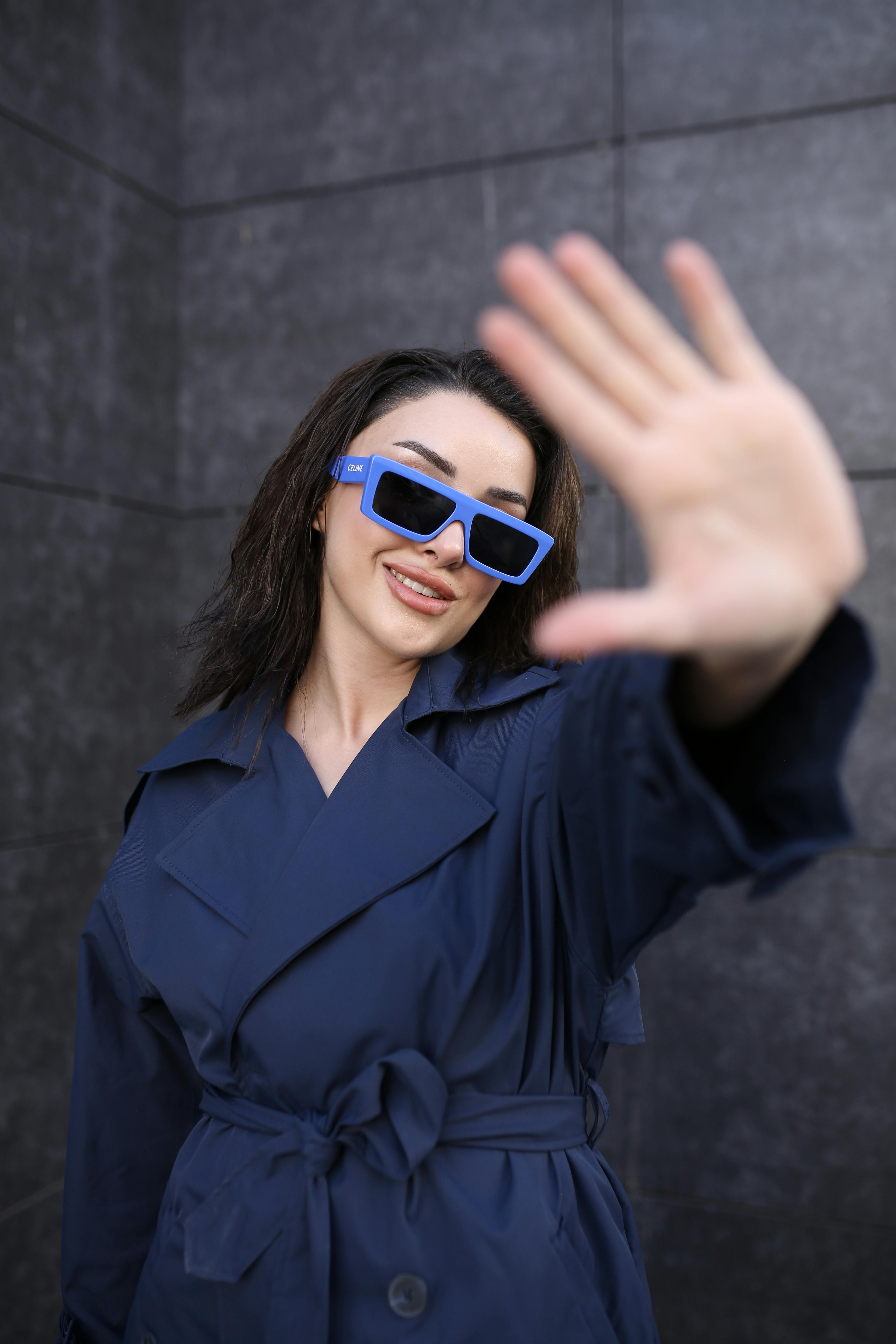 Free Woman in blue trench coat and sunglasses smiling and posing outdoors. Stock Photo