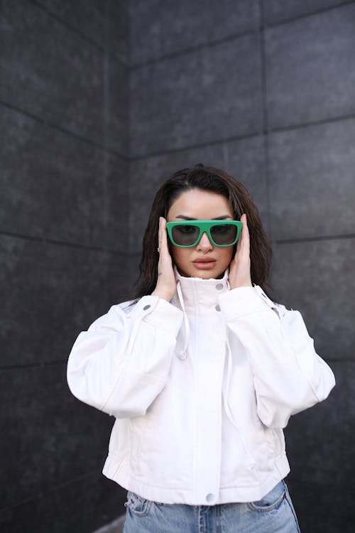 Young Brunette Woman in a White Jacket Holding Green Sunglasses