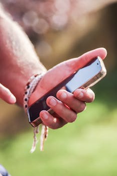 A close-up image of a person holding a smartphone in their hand, illuminated by natural sunlight.
