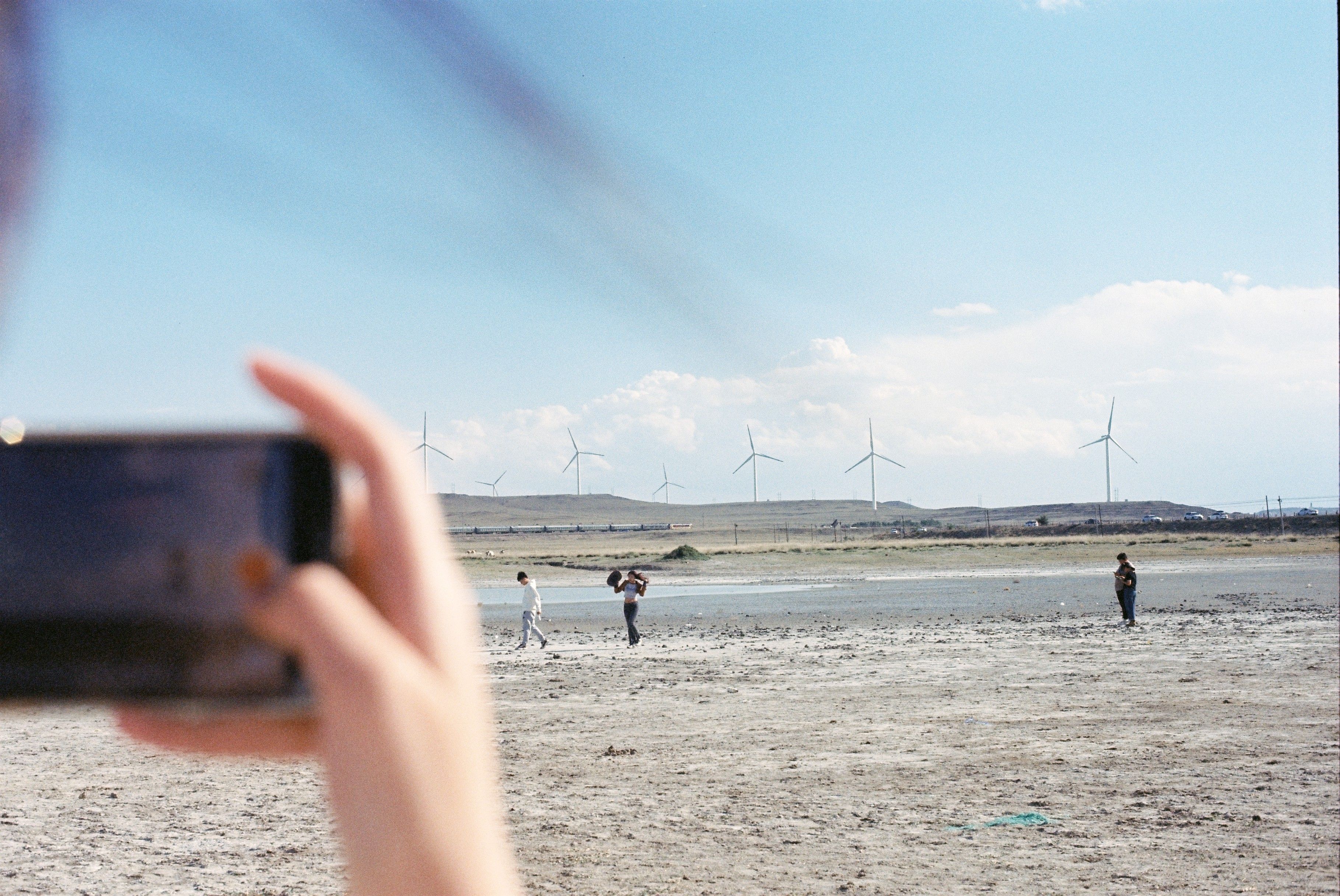 A smartphone captures people walking near wind turbines in a barren landscape.