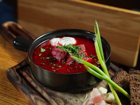 A vibrant beetroot soup topped with fresh herbs and cream, served in a black bowl.