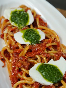 Close-up of spaghetti topped with pesto, mozzarella, and dried tomatoes, beautifully presented.