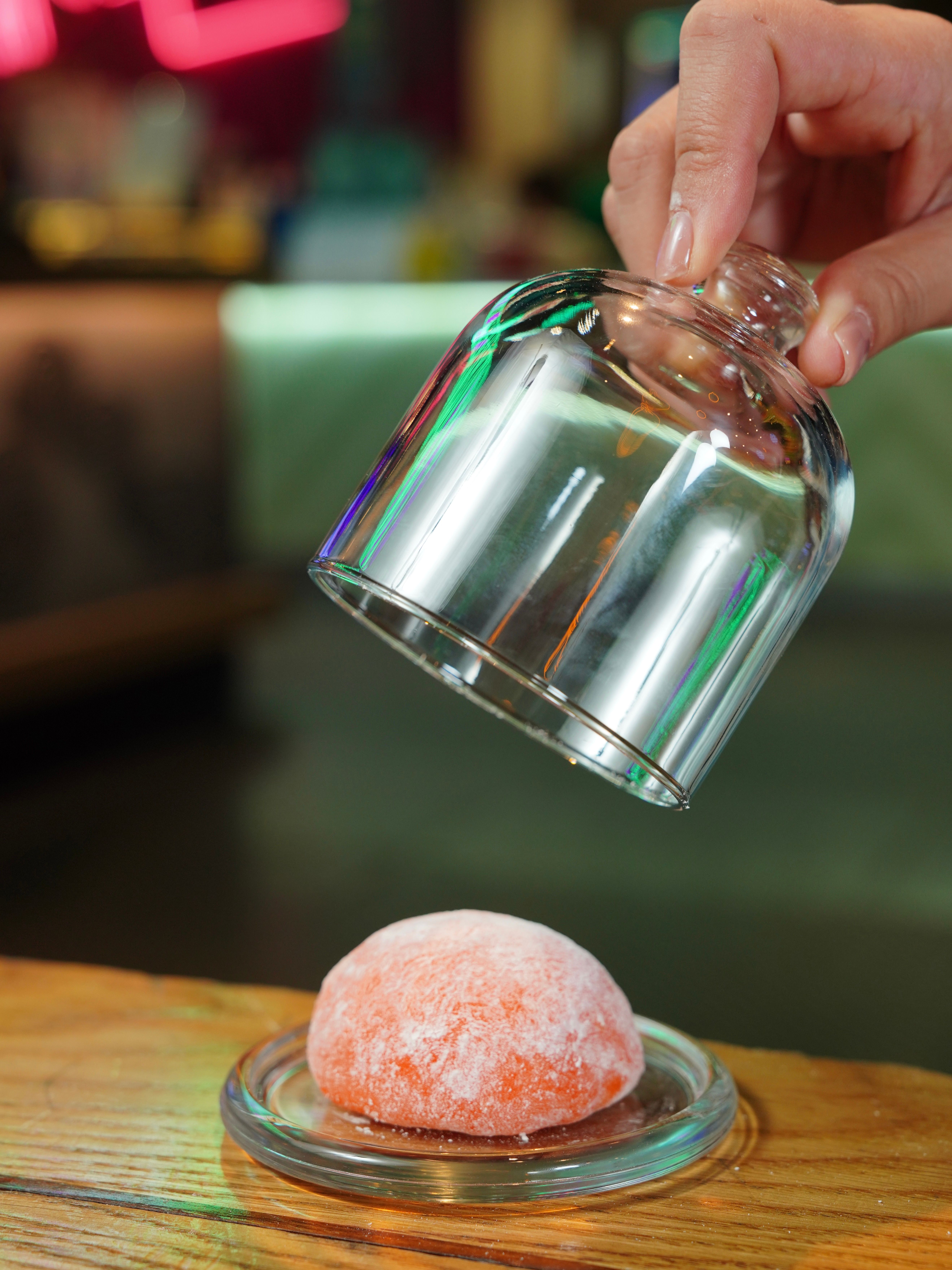 A mochi dessert on a plate covered by an elegant glass dome indoors.