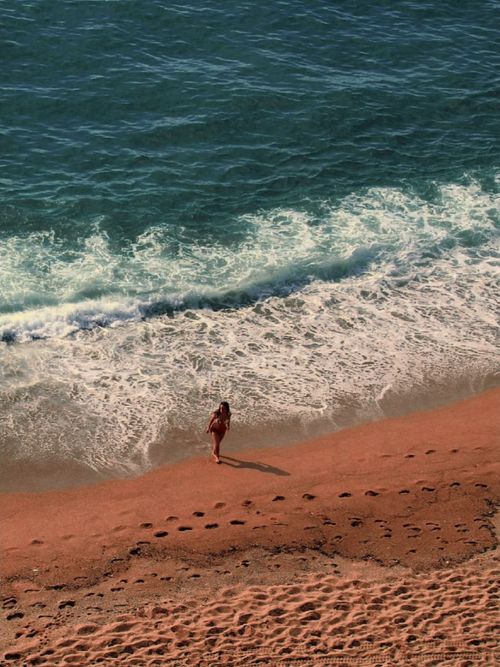Free A woman walks along the vibrant ocean shore as waves gently touch the sandy beach, perfect summer relaxation. Stock Photo