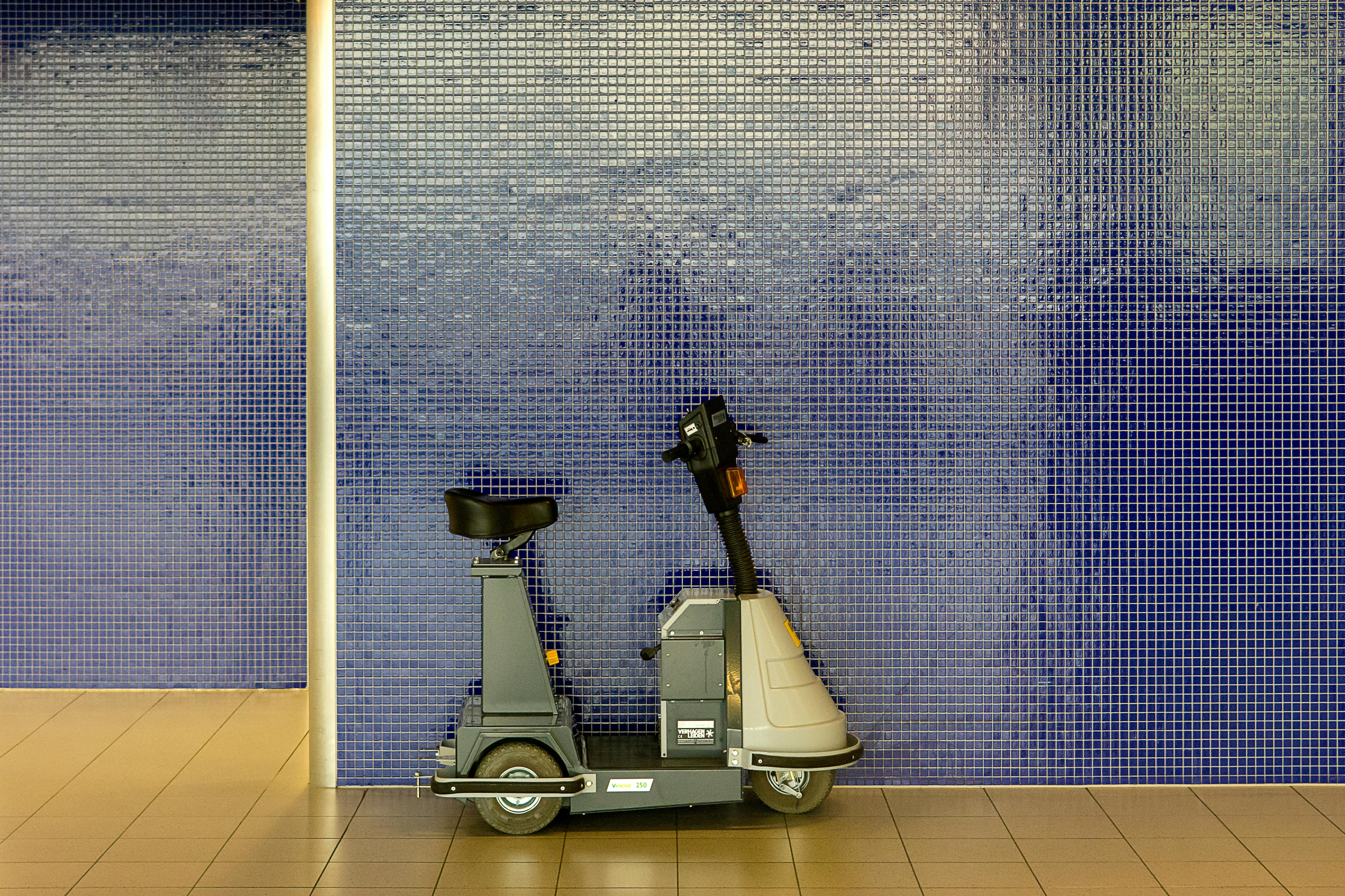 A mobility scooter stands parked against a blue tiled wall, showcasing modern design.