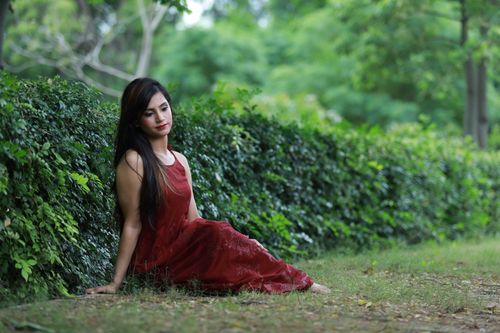 Free A woman in a burgundy dress poses gracefully against a backdrop of lush greenery. Stock Photo