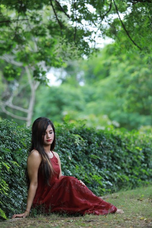 Free A woman in a burgundy dress sits calmly in a lush green park, surrounded by nature. Stock Photo