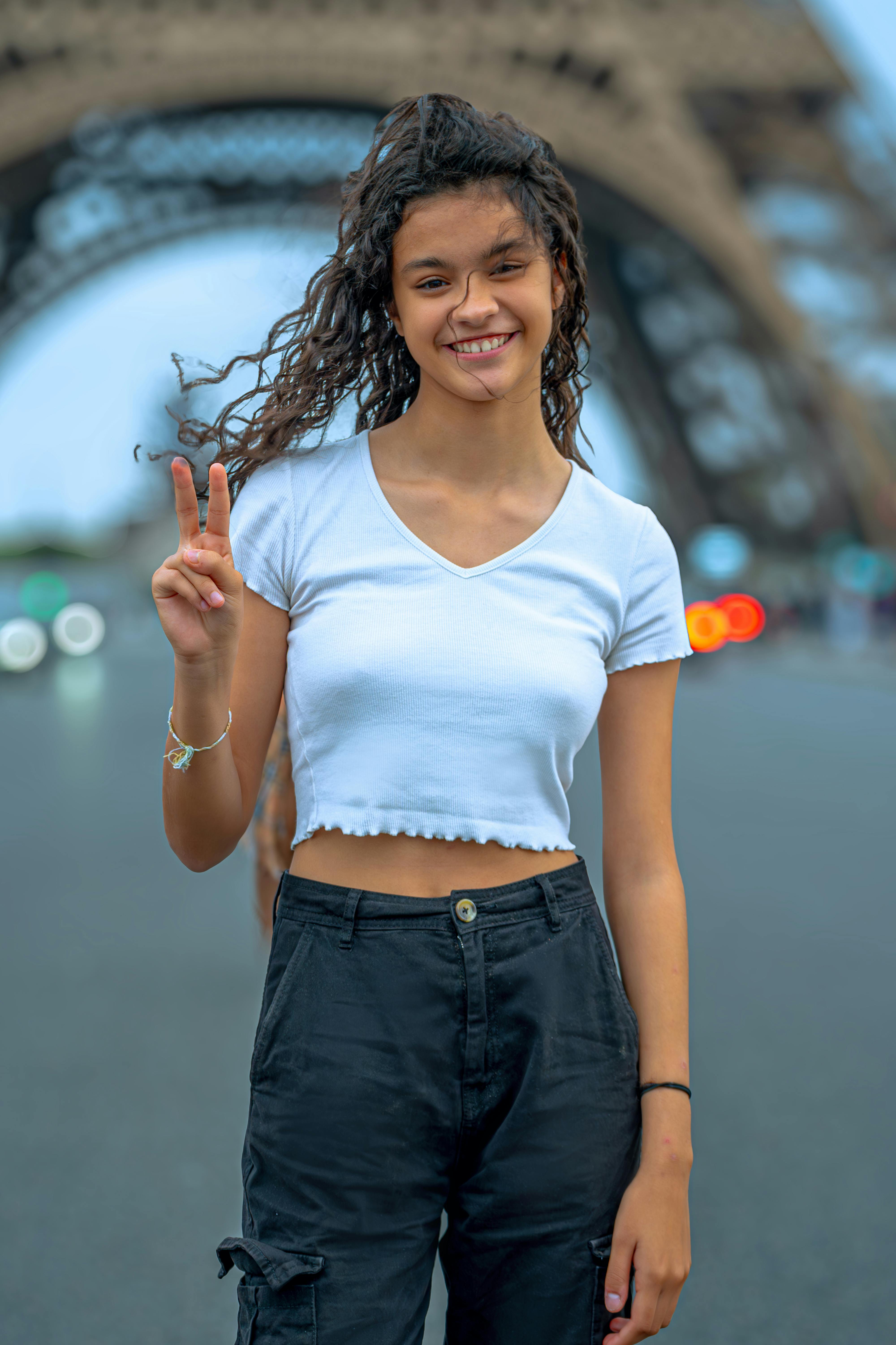 Smiling young woman poses with peace sign in front of the Eiffel Tower in Paris, France.