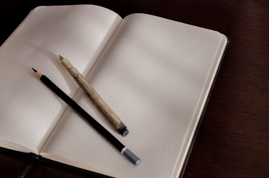 Dotted open notebook with mechanical pencil and traditional pencil on a dark wooden desk.