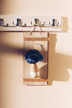 A minimalist wooden wall hanging featuring a blue flower, illuminated by sunlight.