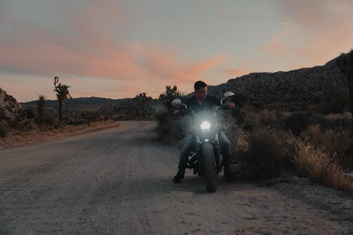 Biker on a Motorcycle Standing on the Side of a Gravel Road Through the Desert